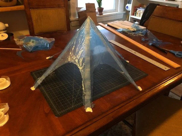 Partially assembled translucent blue kite on a cutting mat atop a wooden dining table