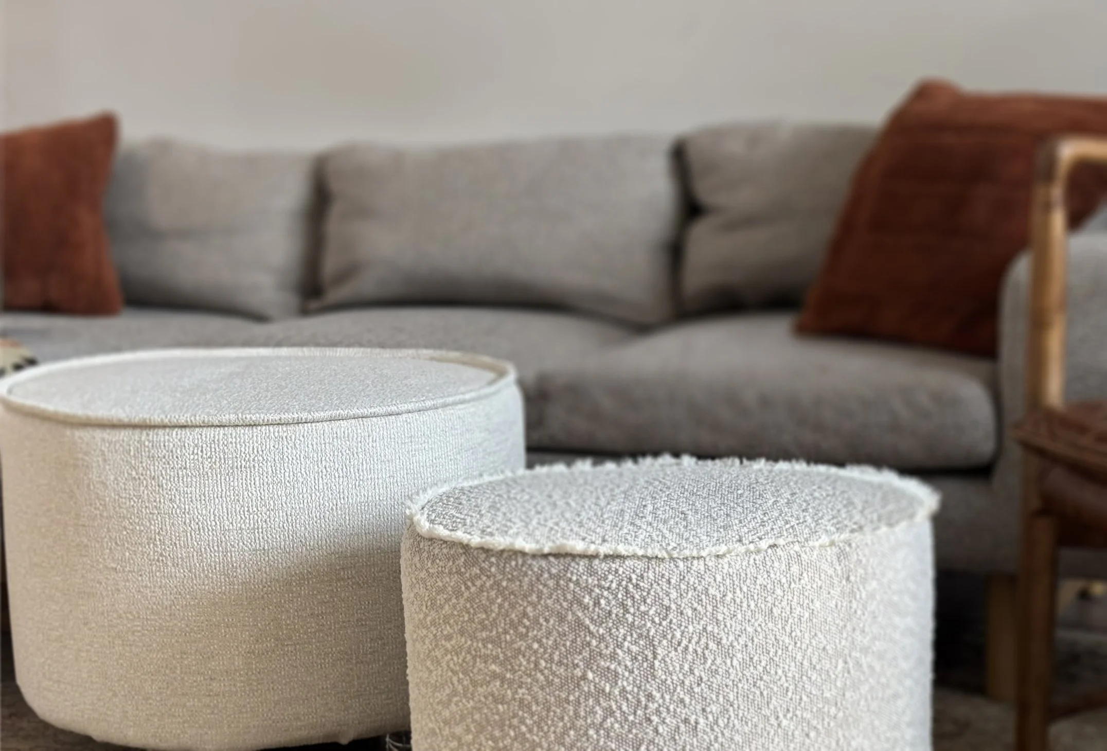 Two round upholstered ottomans in a cozy living room with a gray sofa and brown accent pillows