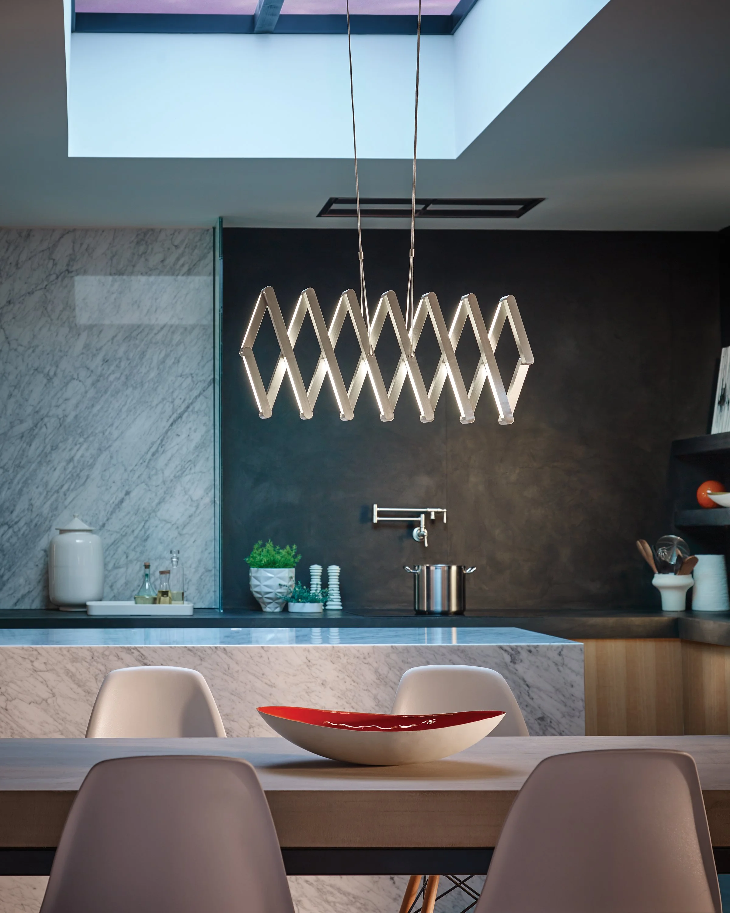 Modern kitchen and dining area with a geometric pendant light, marble island, black backsplash, bar stools, and decorative bowl