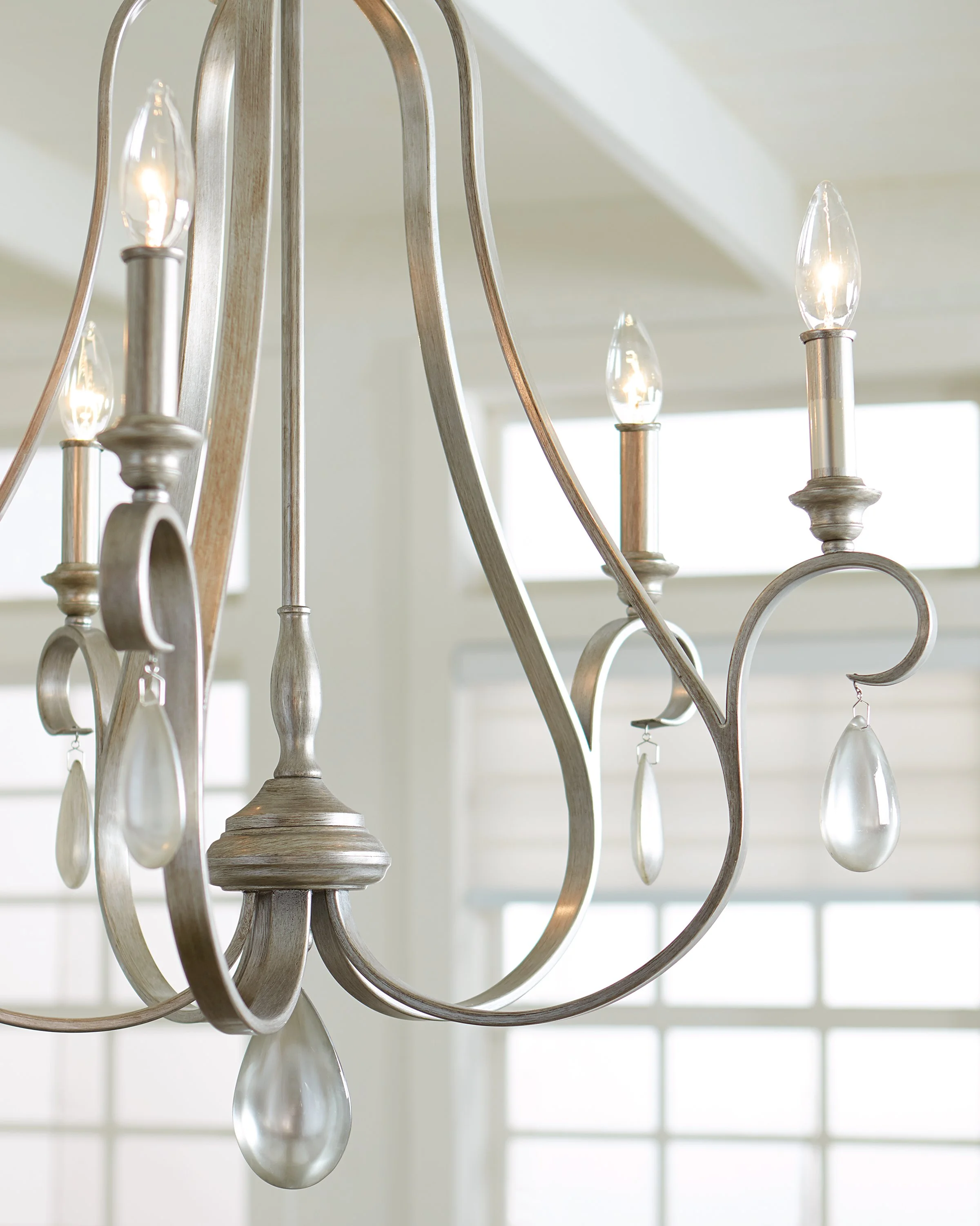 Close-up of a rustic silver chandelier with curved arms, lit candle-shaped bulbs, and hanging glass teardrop crystals