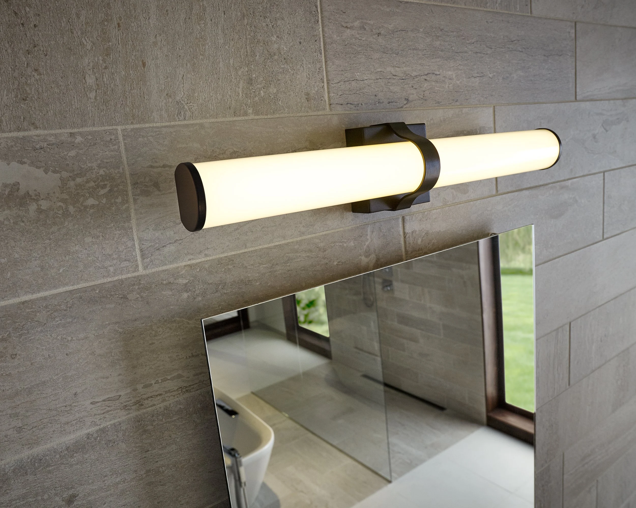 Modern horizontal wall sconce with a frosted cylindrical shade above a bathroom mirror