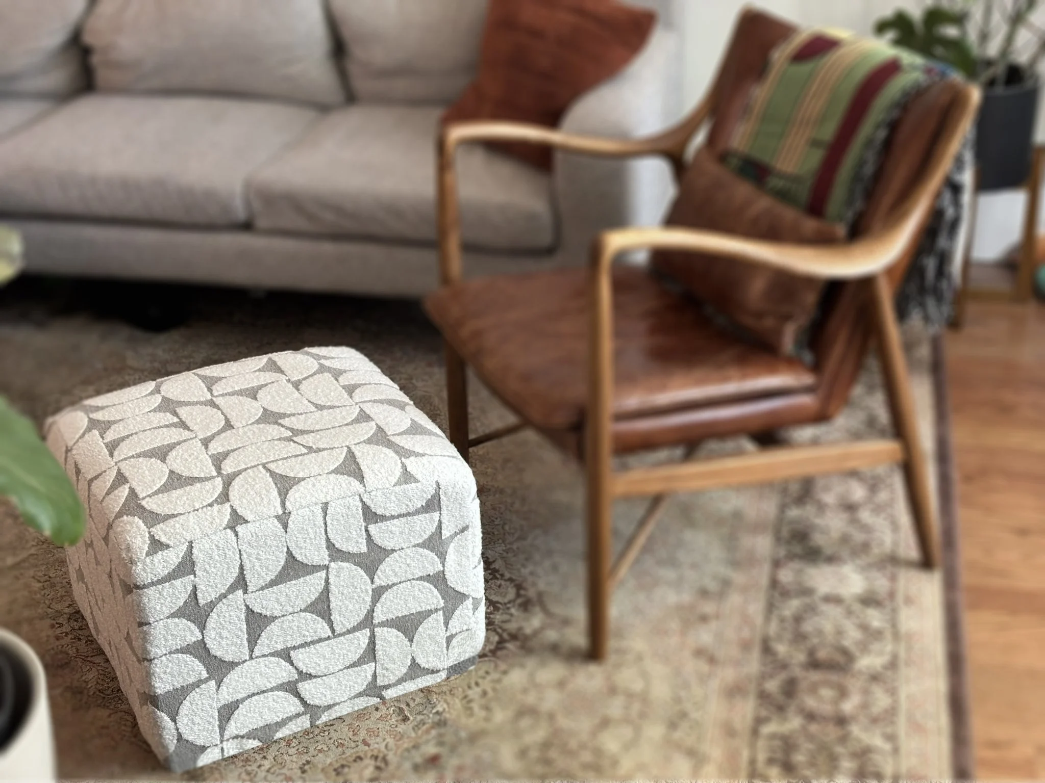 Mid-century modern living room with a patterned ottoman, leather armchair, sofa, colorful pillows, and area rug