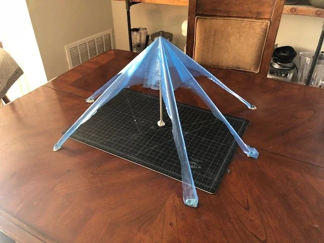 Blue plastic tent-like structure mounted on a black grid cutting mat atop a wooden table