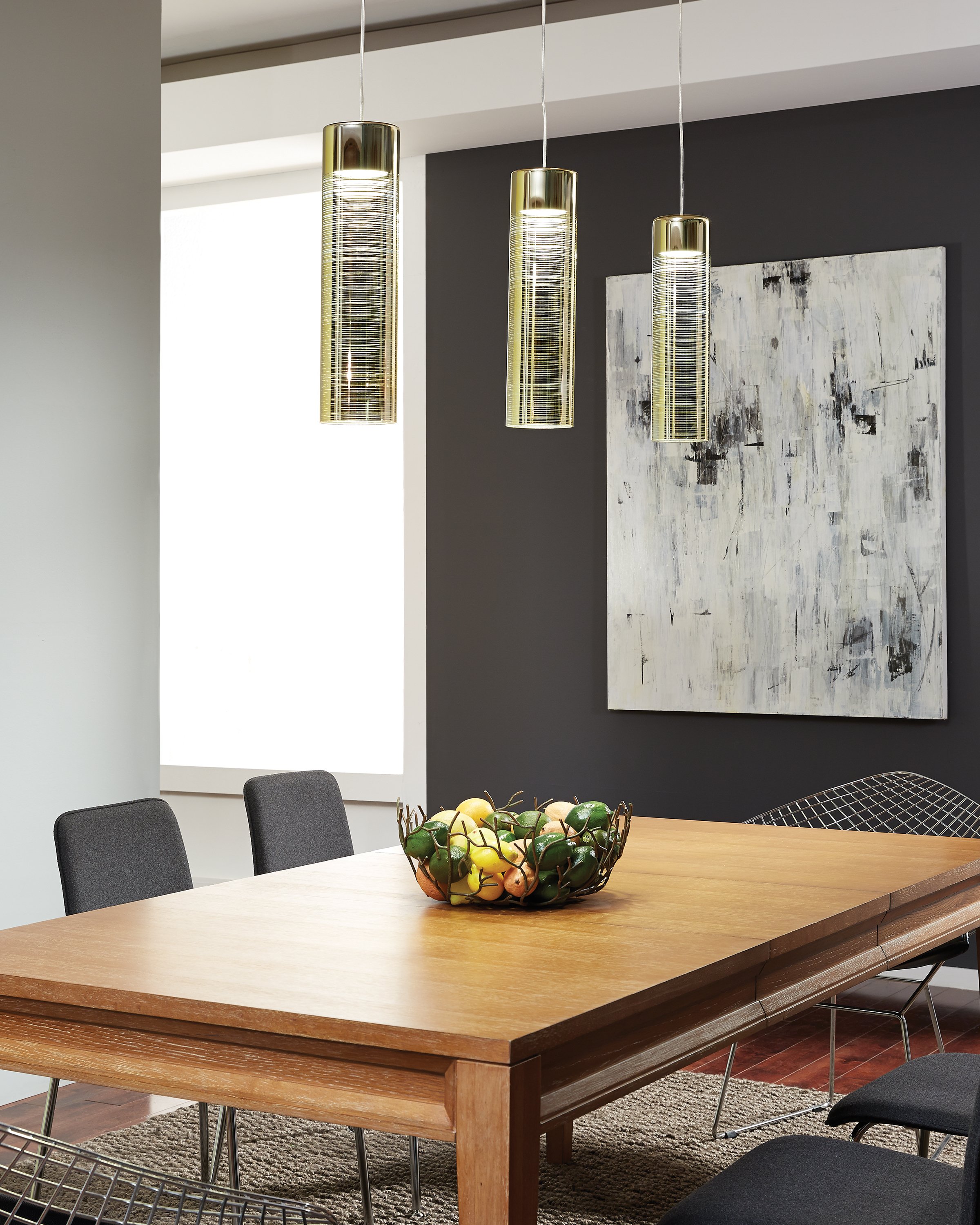 Modern dining room with a wooden table, fruit bowl, three gold pendant lights, black chairs, and abstract wall art