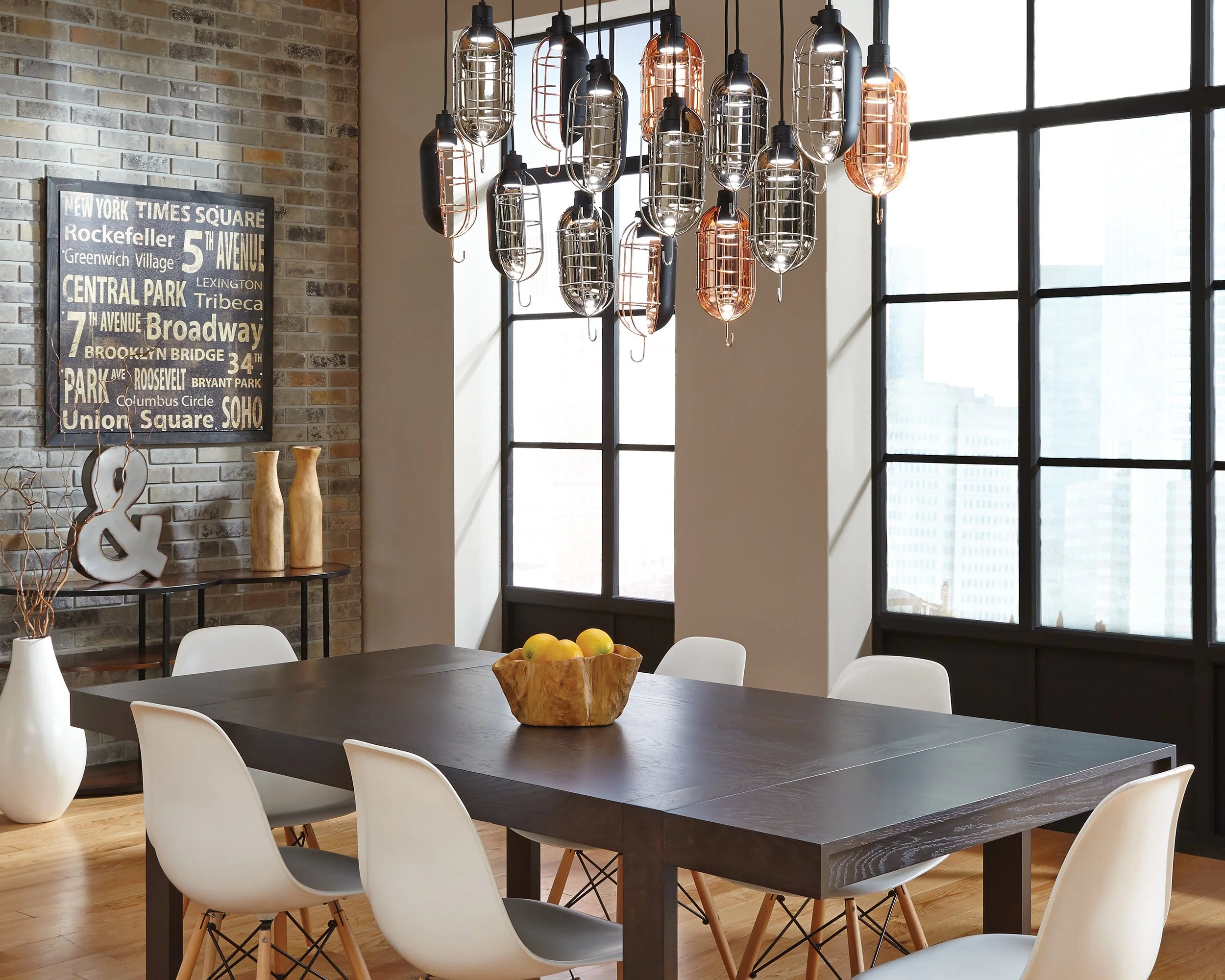 Modern dining room with a dark wood table, white chairs, industrial cage pendant lights, brick accent wall, and large windows