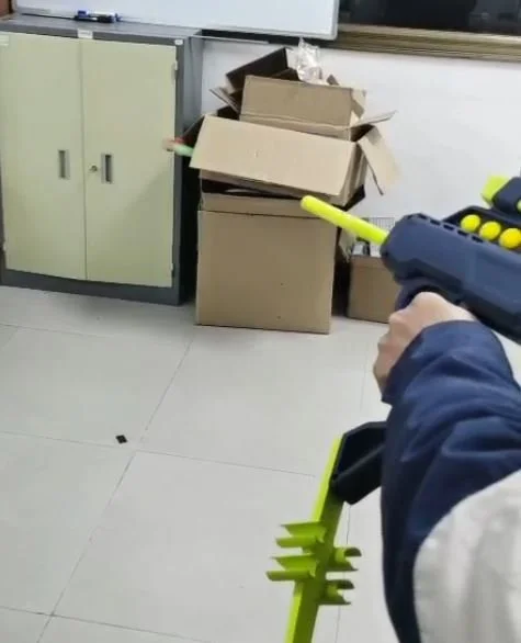 Person holding a blue-and-yellow toy blaster aimed at open cardboard boxes in an office.