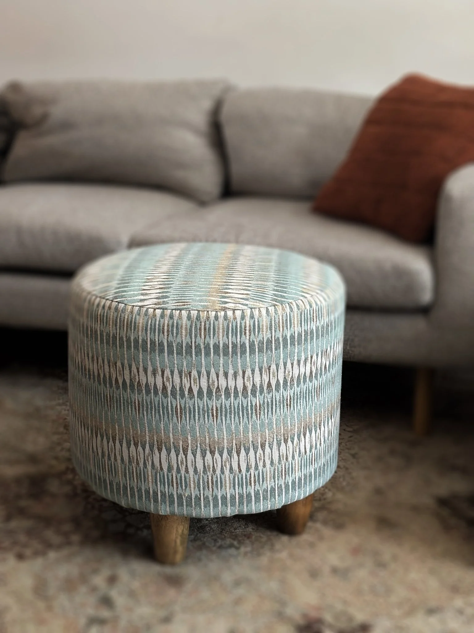 Patterned teal and white upholstered ottoman with wooden legs in front of a sofa