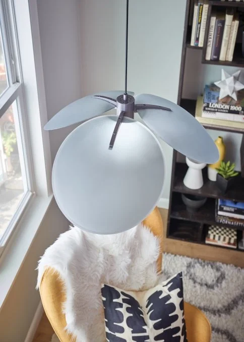 Modern gray pendant ceiling lamp above a white furry lounge chair beside a bookshelf and window