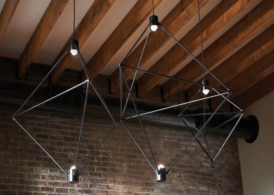 Modern geometric pendant lights hanging from exposed wooden ceiling beams in a brick-walled interior
