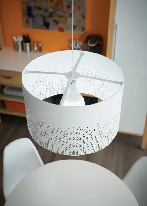 White perforated drum pendant light hanging above a round dining table