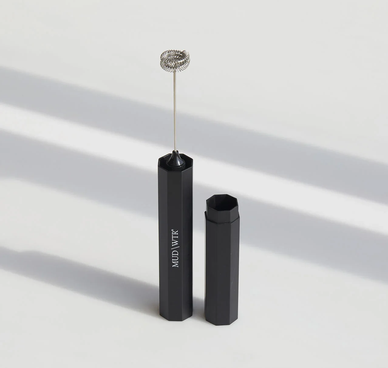 Black MUD\WTR handheld milk frother with its open hexagonal cap beside it