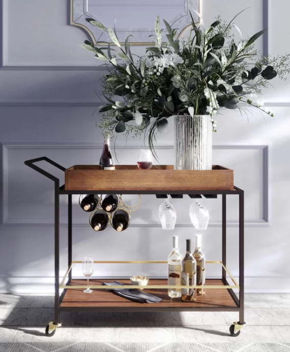 Modern wooden and black metal bar cart with wine bottles, hanging wine glasses, cocktail glasses, and a large floral arrangement in a vase