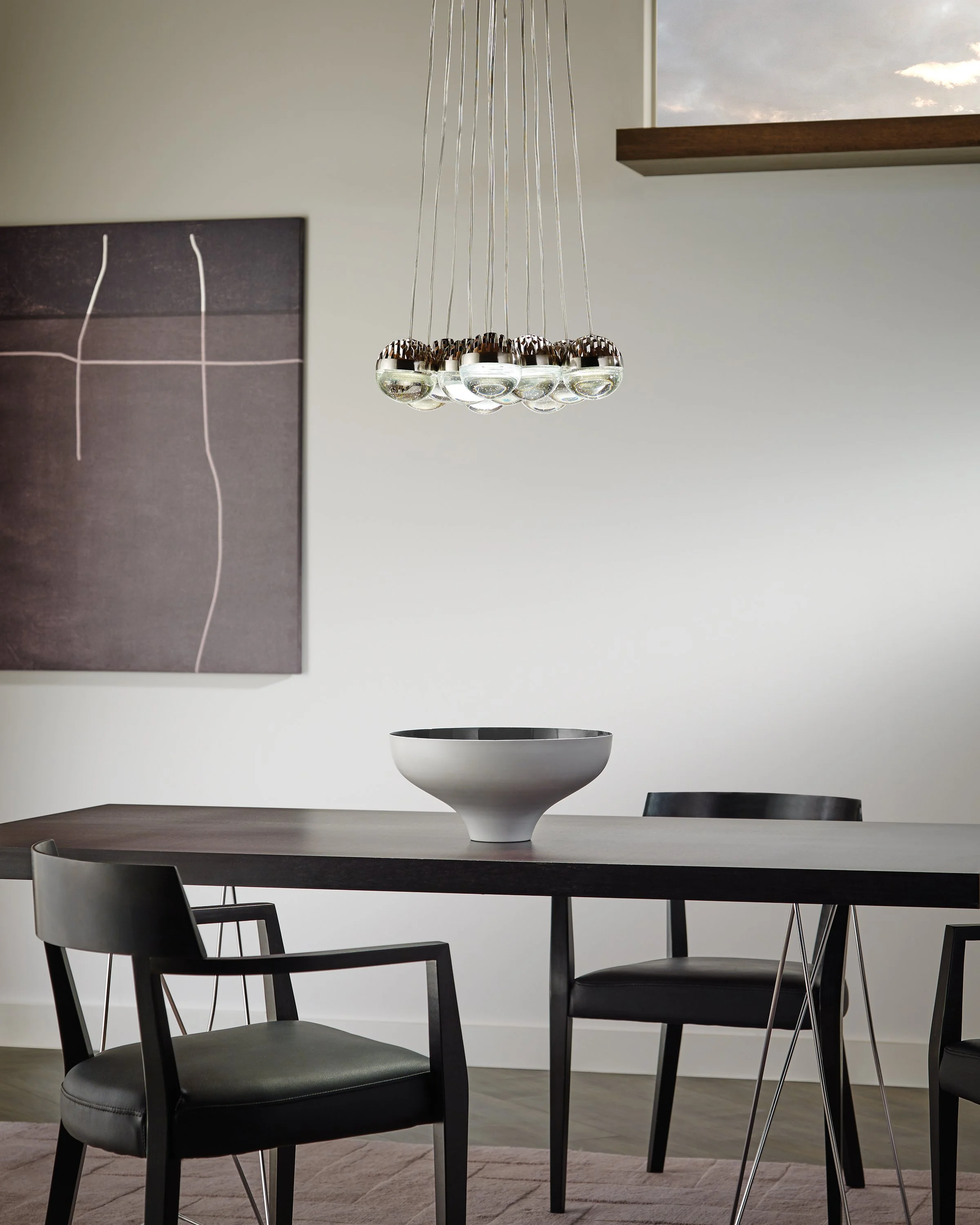 Modern dining room with a chrome and glass pendant light above a dark wood table, black chairs, and a decorative bowl