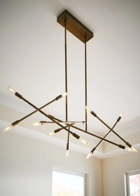 Modern brass multi-arm chandelier with exposed bulbs hanging from a rectangular wood ceiling mount