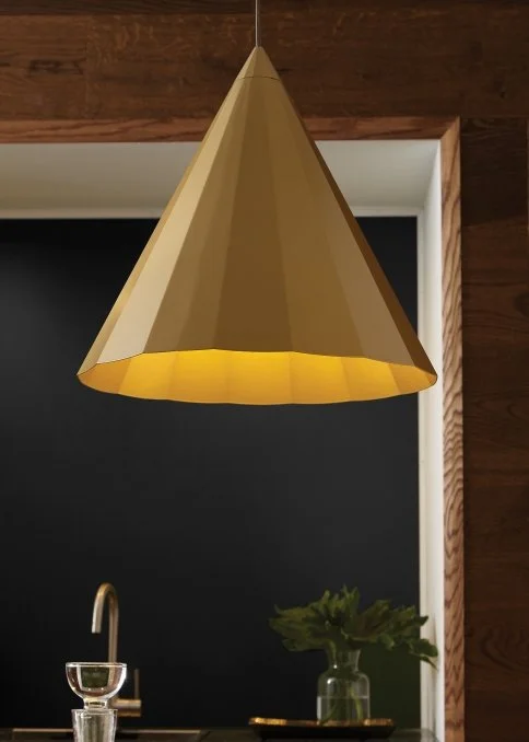 Modern gold cone-shaped pendant light glowing above a kitchen counter with a faucet and potted plant