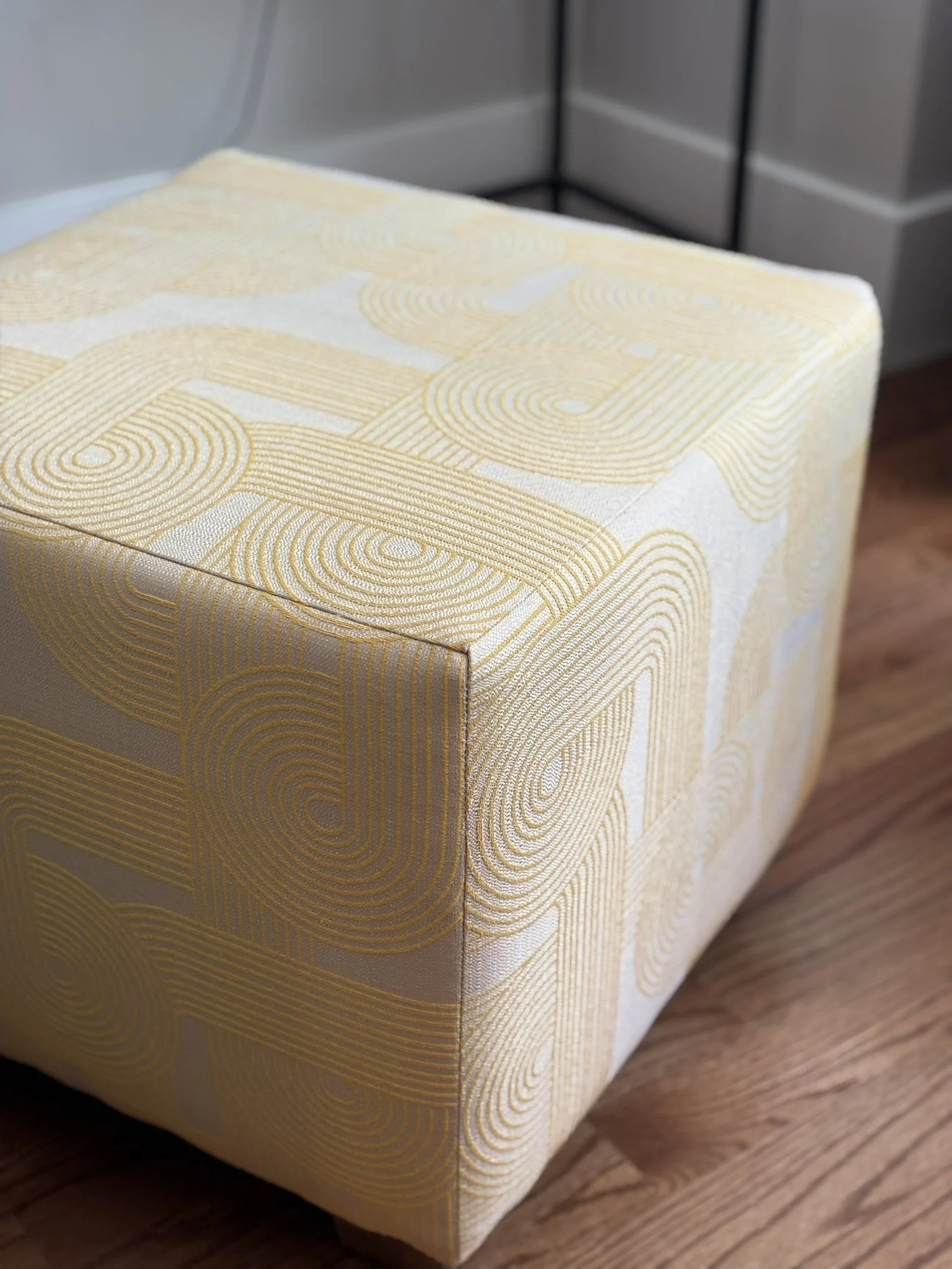 Close-up of a cream upholstered ottoman with a gold geometric pattern on a hardwood floor