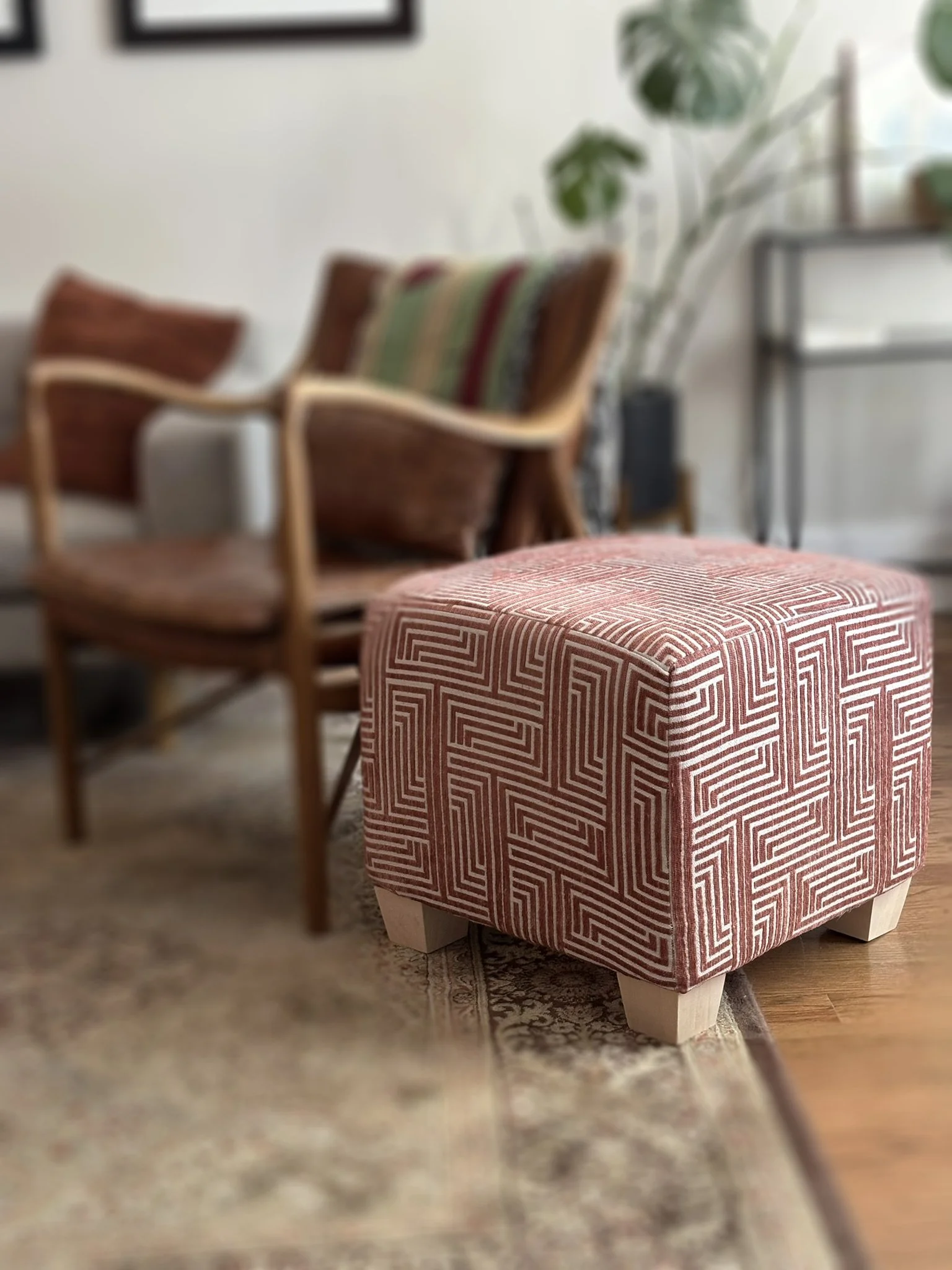 Red and white geometric-patterned ottoman with wooden legs in a living room