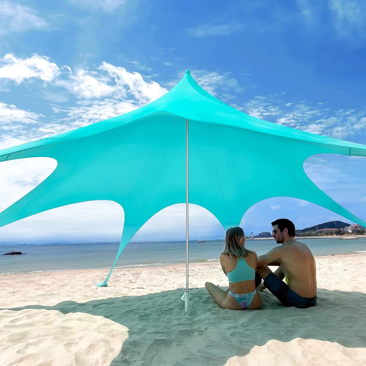 Couple relaxing under a turquoise shade canopy on a sandy beach by the ocean