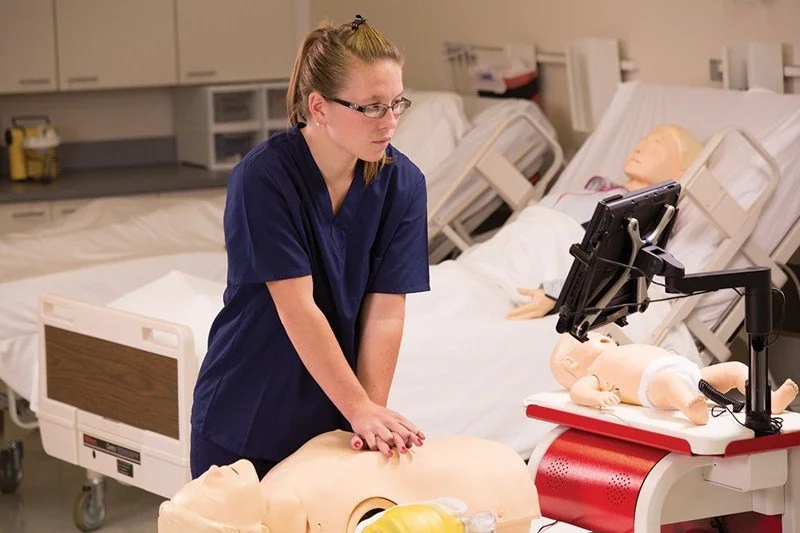Nursing student practicing CPR on a medical training mannequin in a hospital simulation lab
