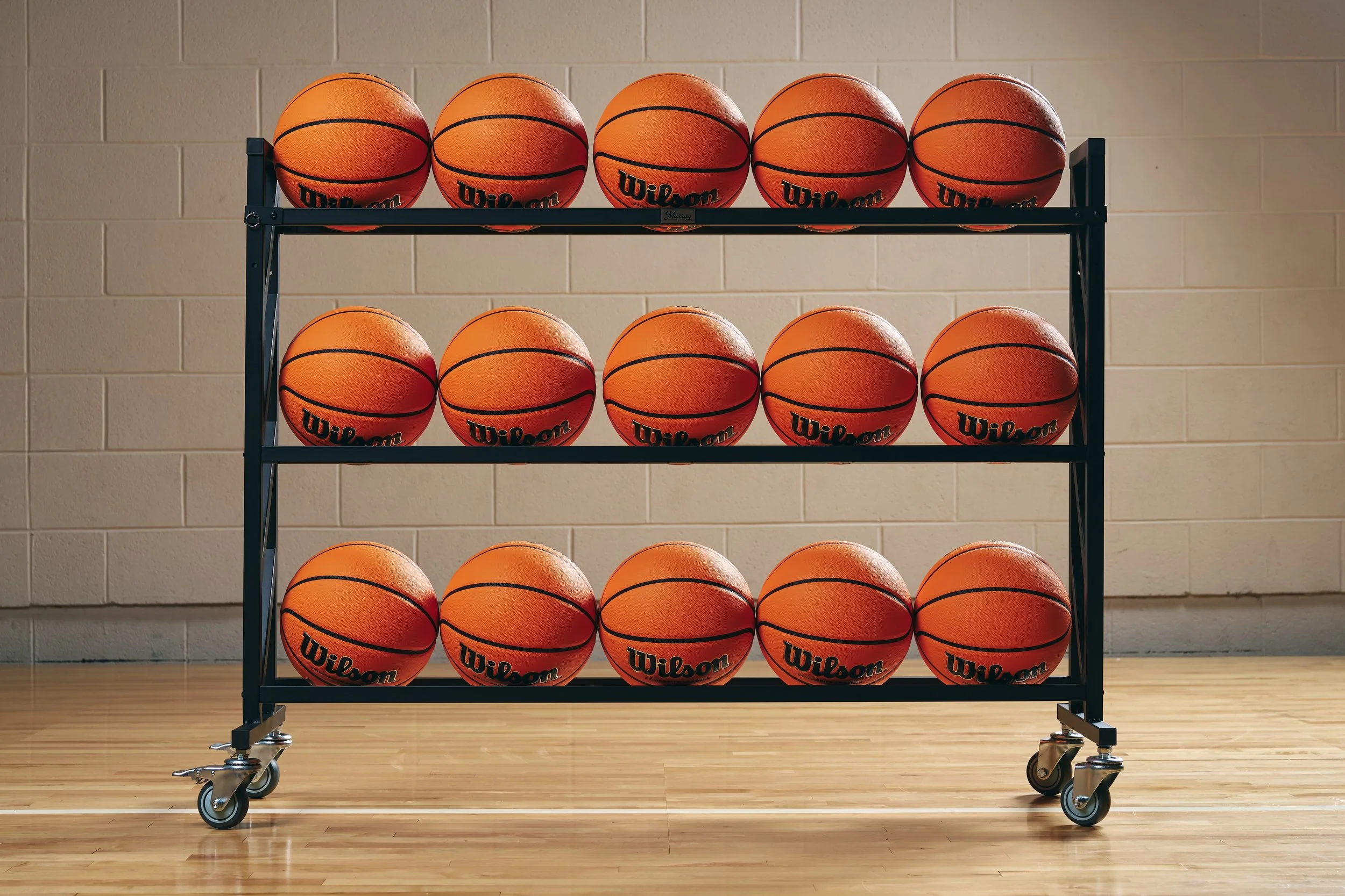 Rows of orange Wilson basketballs on a black rolling rack in a gymnasium