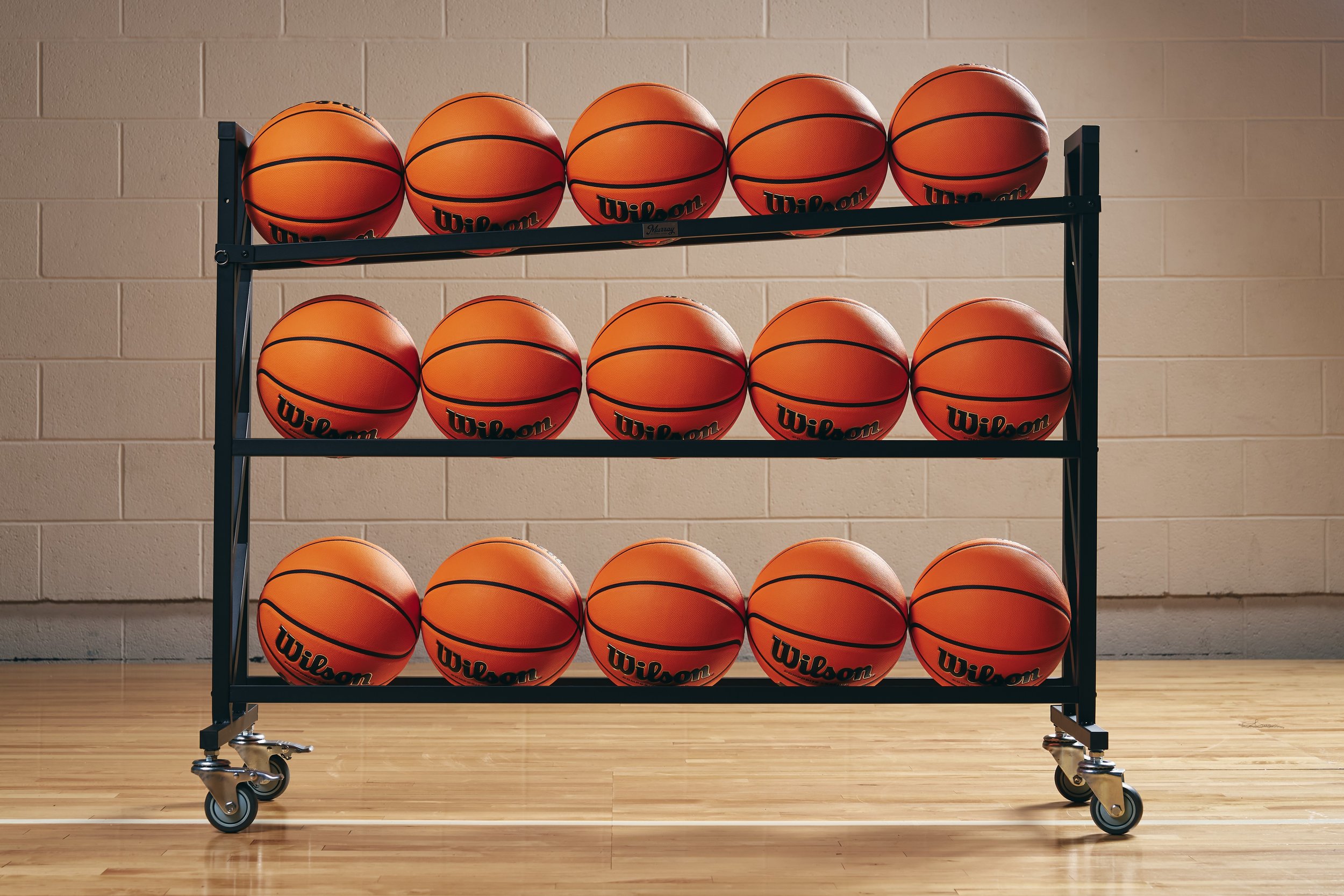 Rolling black metal rack filled with rows of orange Wilson basketballs in a gymnasium