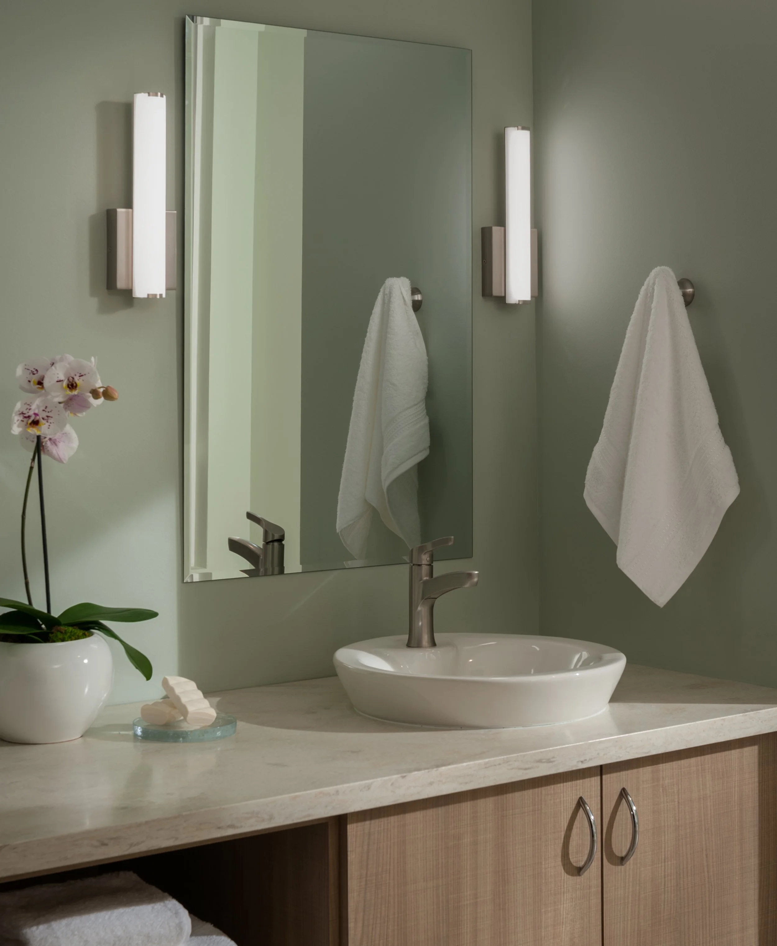 Modern bathroom vanity with vessel sink, large mirror, wall sconces, white towels, and orchid plant