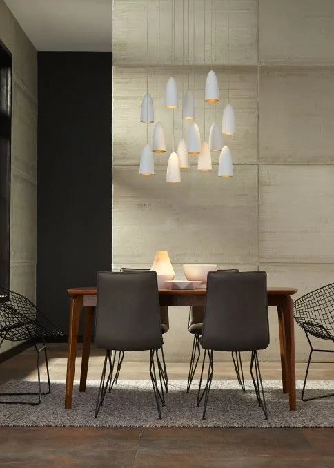 Modern dining room with a wooden table, four black chairs, sculptural pendant lights, and textured concrete walls