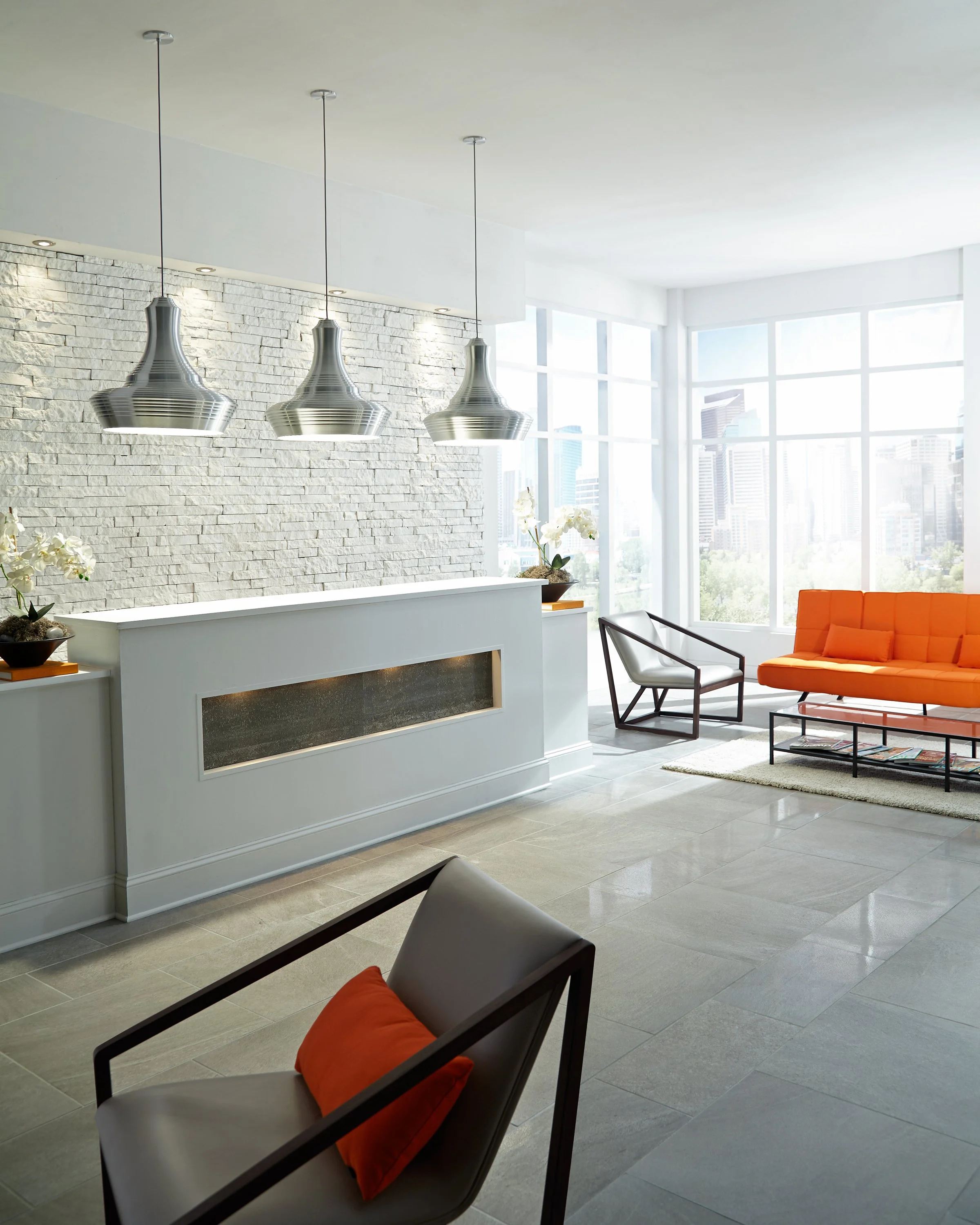 Modern living room with a stone fireplace, three pendant lights, orange sofa, armchairs, and floor-to-ceiling city-view windows