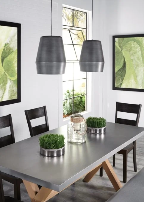 Modern dining room with a gray table, black chairs, pendant lights, potted grass, and abstract wall art