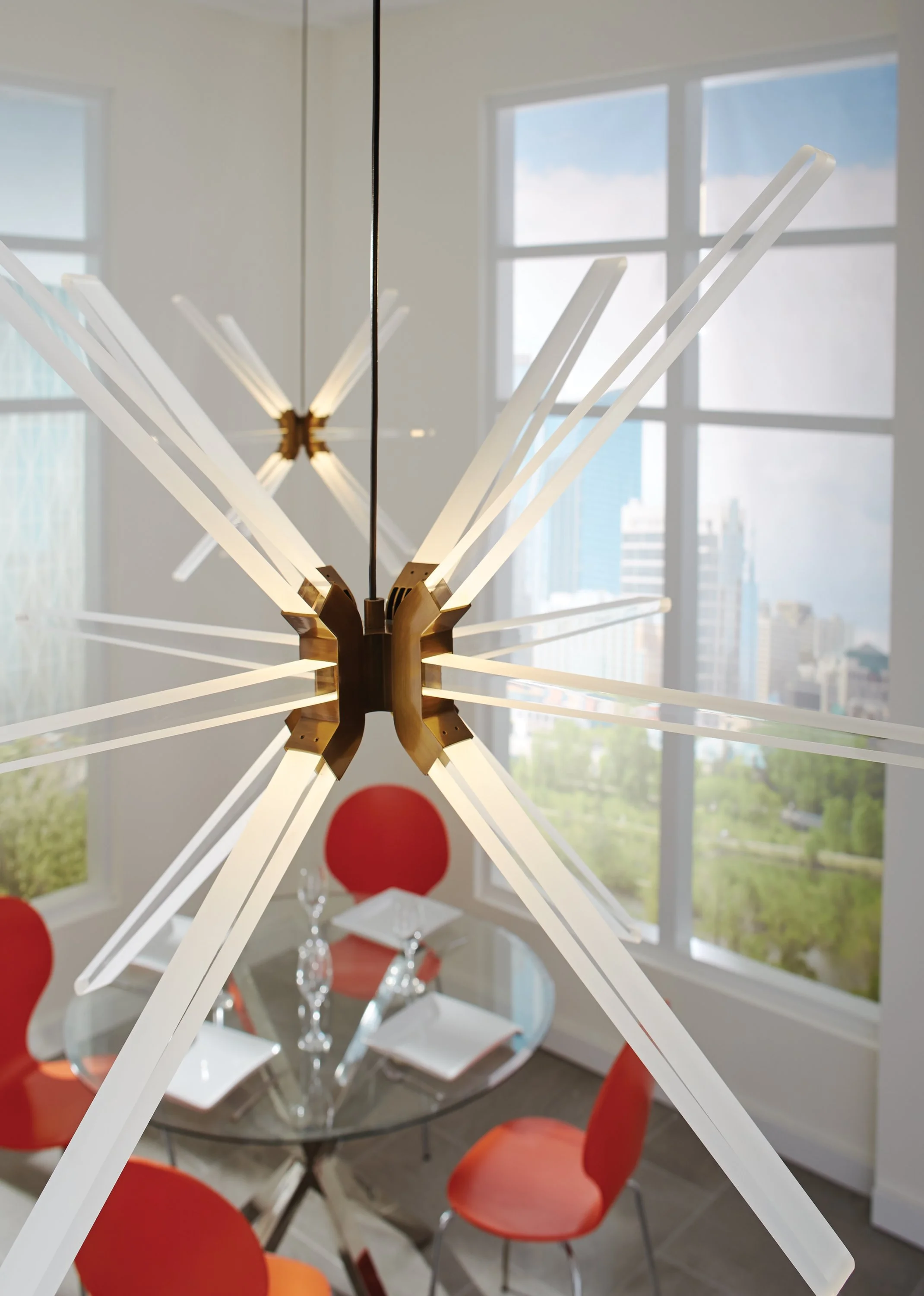 Modern brass starburst chandelier with white illuminated arms in a bright dining room with red chairs and large windows