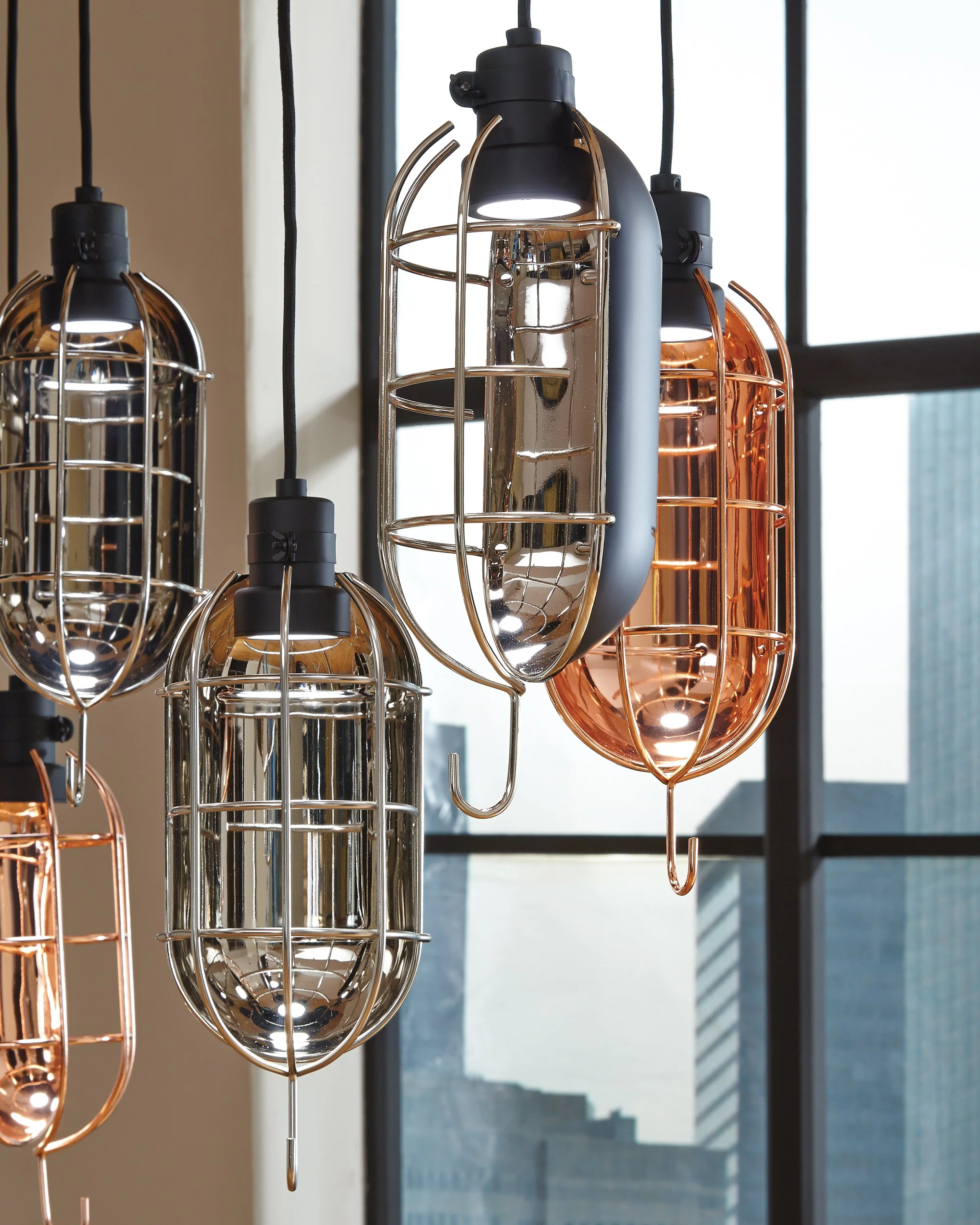 Modern industrial pendant lights with chrome and copper finishes hanging in front of large windows