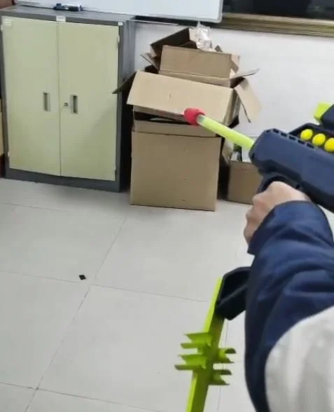 Person aiming a toy blaster at stacked cardboard boxes indoors