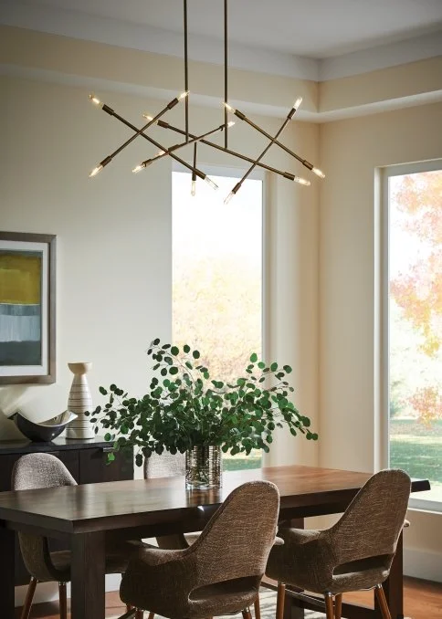 Modern dining room with a dark wood table, upholstered chairs, leafy centerpiece, large windows, and sculptural linear chandelier