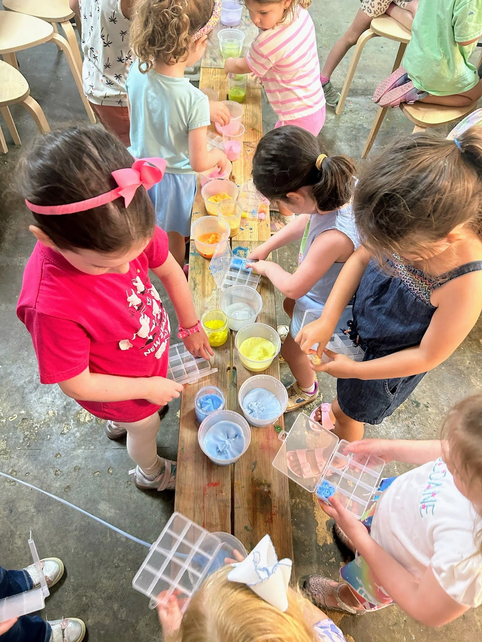 Children gathered around a wooden table with containers of colorful slime, engaging in a slime-making activity.