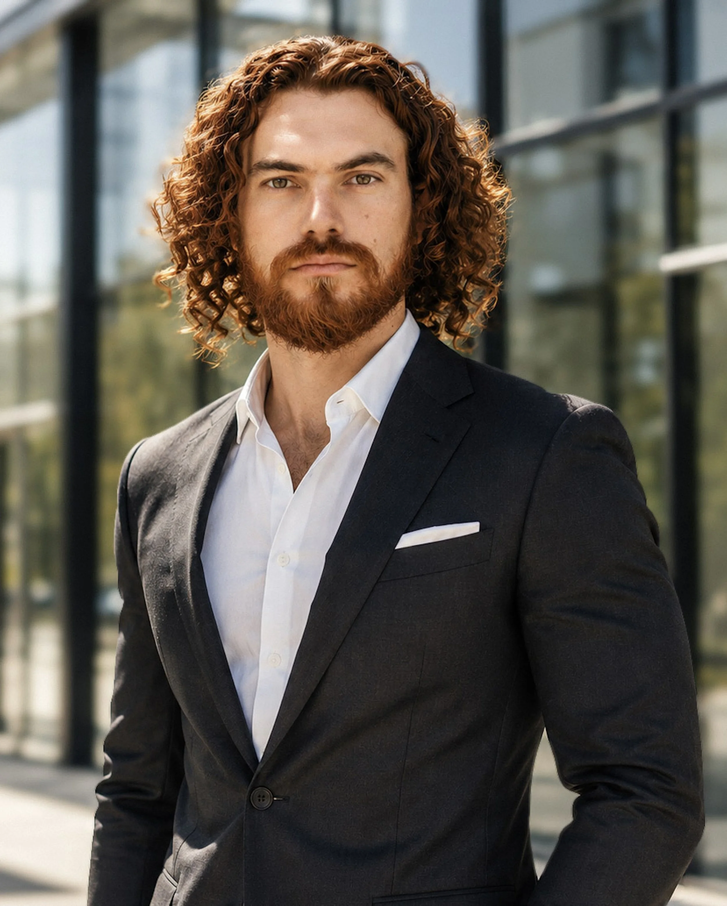 Professional environmental headshot of a man in a black suit photographed outdoors near a modern building.
