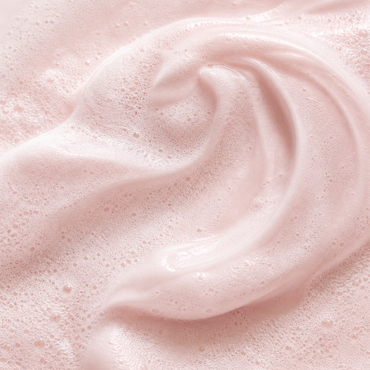 Close-up of a swirled dollop of light pink mousse or whipped cream with foam bubbles.