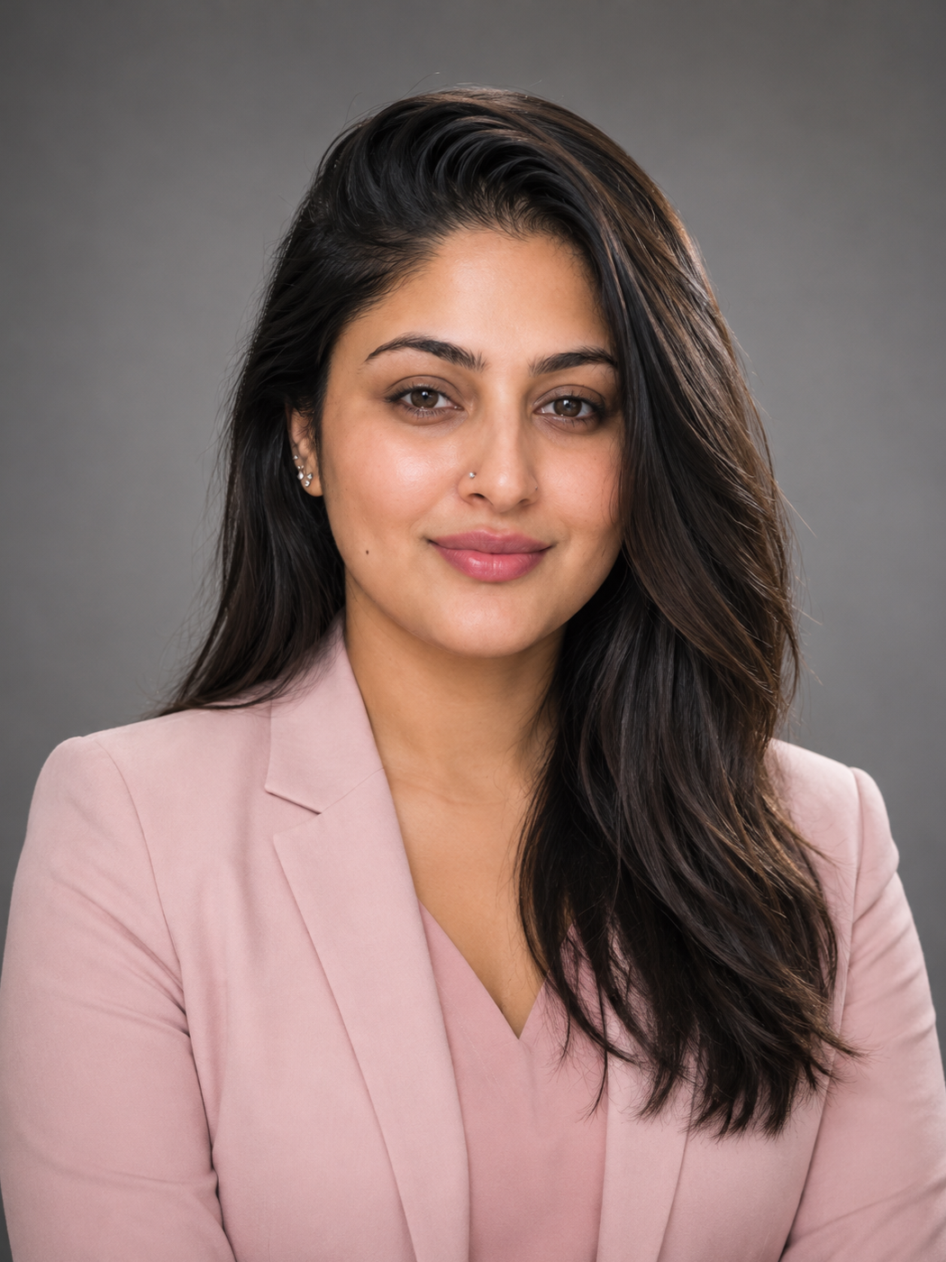Headshot of a woman with long dark hair wearing a light pink blazer, posing against a neutral background.