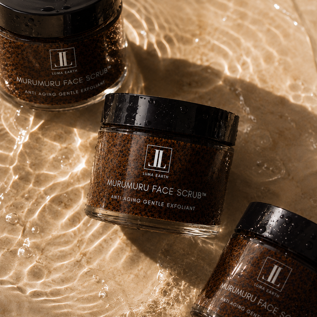 Three jars of Luma Earth Murumuru Face Scrub placed on a sandy surface with water and light reflections.
