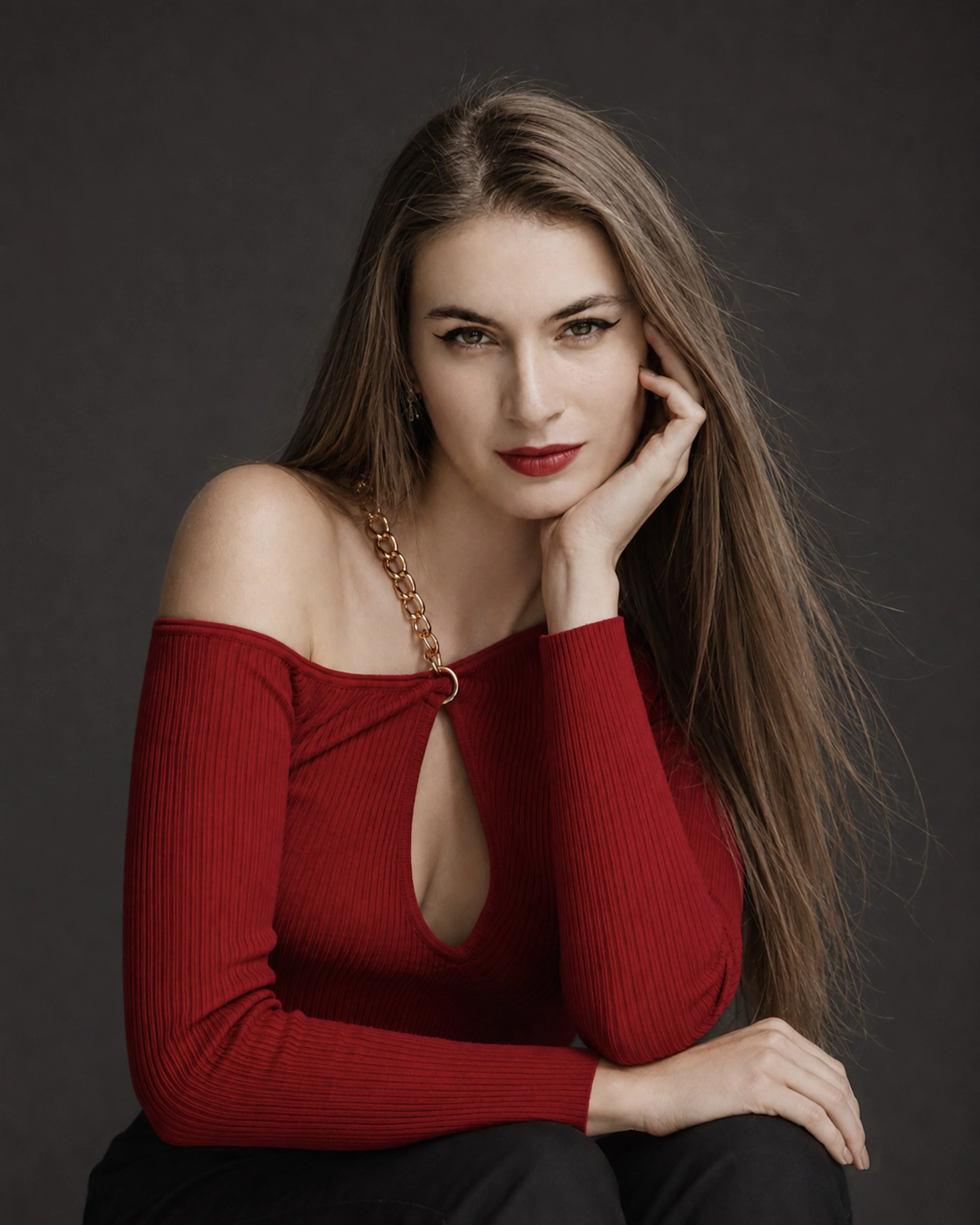 Personal branding portrait of a woman in a red top posing against a dark studio background.