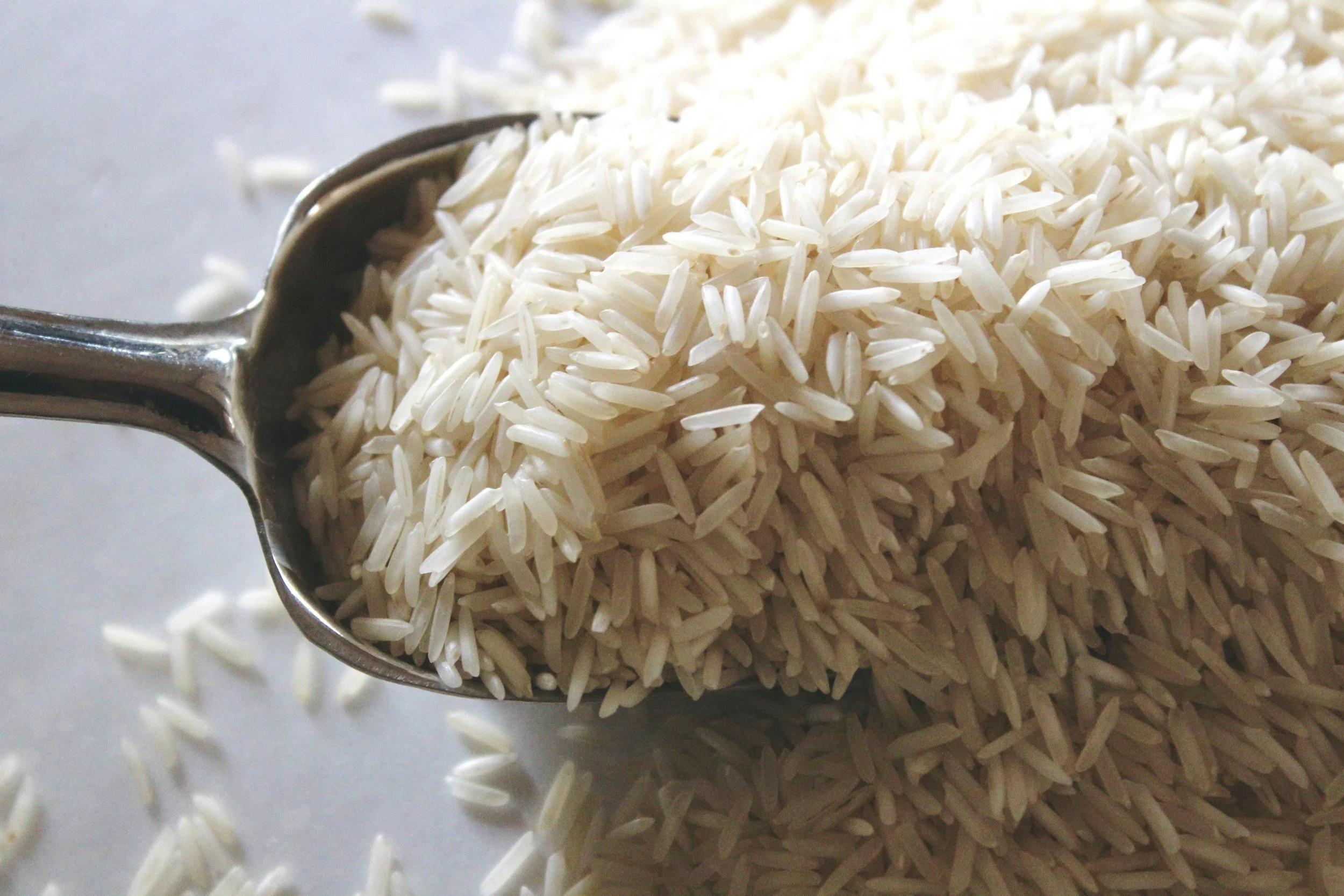 Close-up of uncooked white rice spilling from a metal measuring scoop.