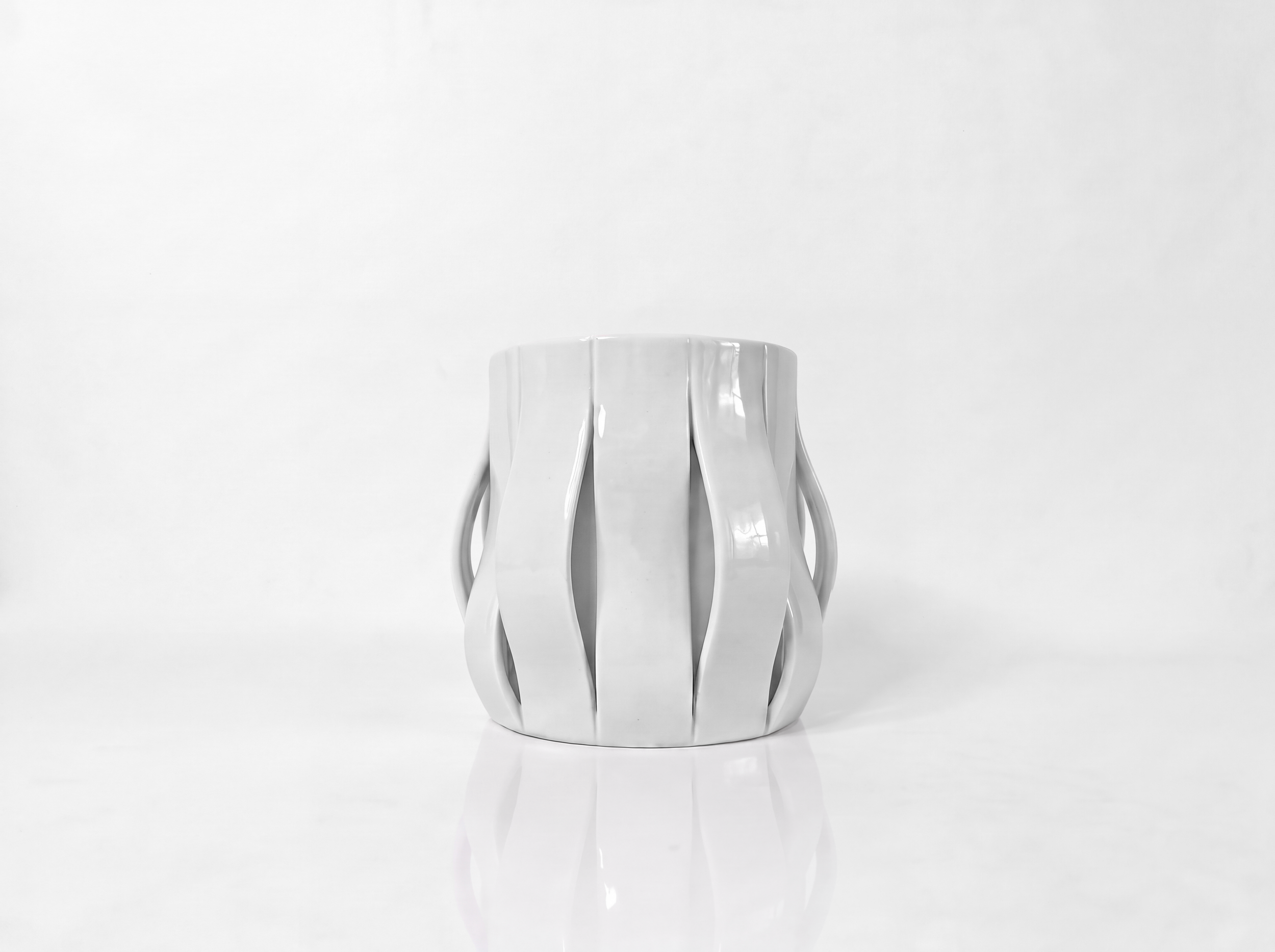 Finger Wave Mug by Pheiffer — a white glazed ceramic vessel with vertical ribs that split and curve away from the body to form open handles on both sides.