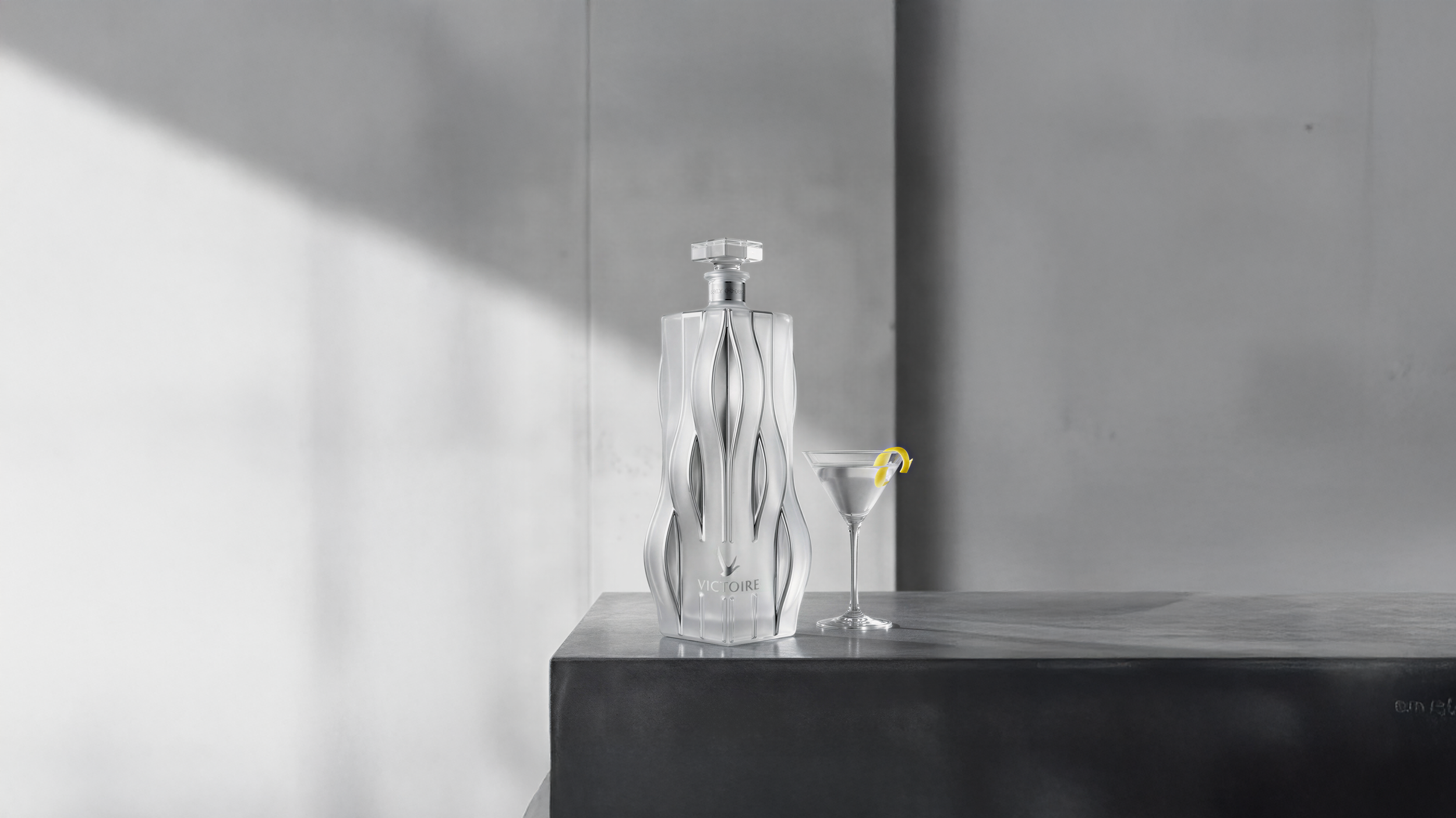 Victoire bottle concept proposal by Pheiffer — a faceted frosted glass vodka bottle with vertical sculpted ribs, shown on a dark concrete plinth beside a martini with a lemon twist.