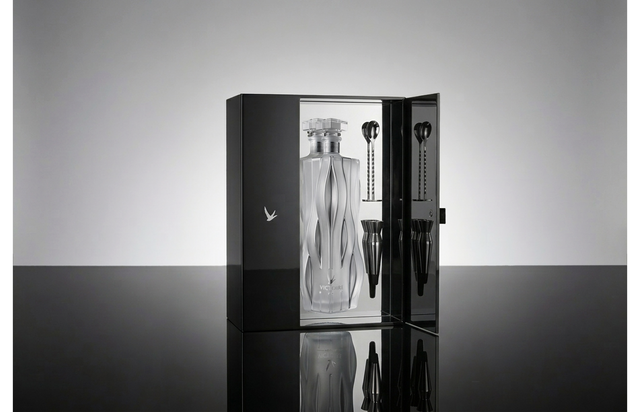 Victoire packaging concept by Pheiffer — a black lacquered presentation case opening to reveal the sculpted bottle flanked by bar tools, shown in reflection.