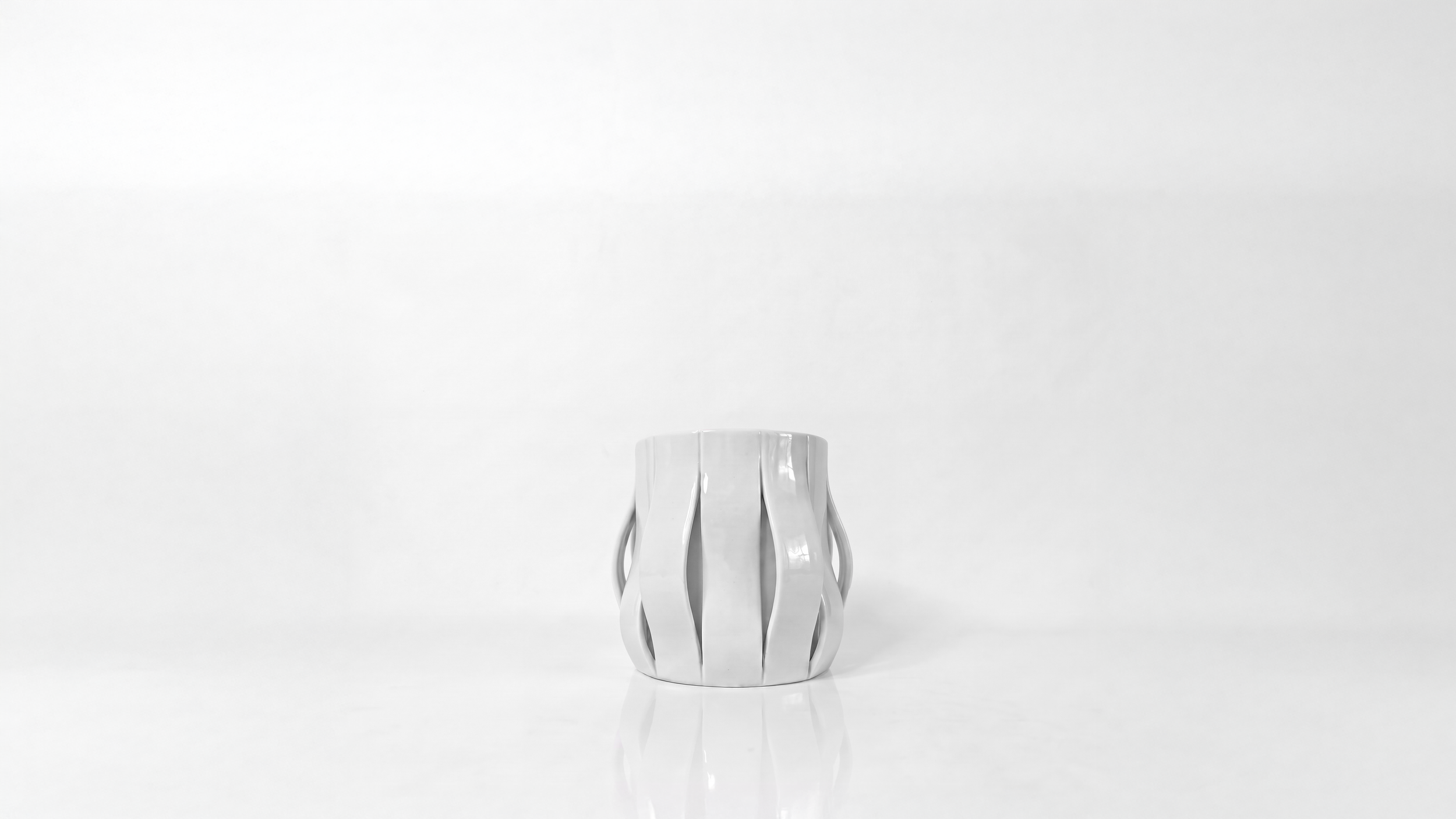 Finger Wave Mug by Pheiffer — a white glazed ceramic vessel with vertical ribs that split and curve outward to form open handles on both sides.