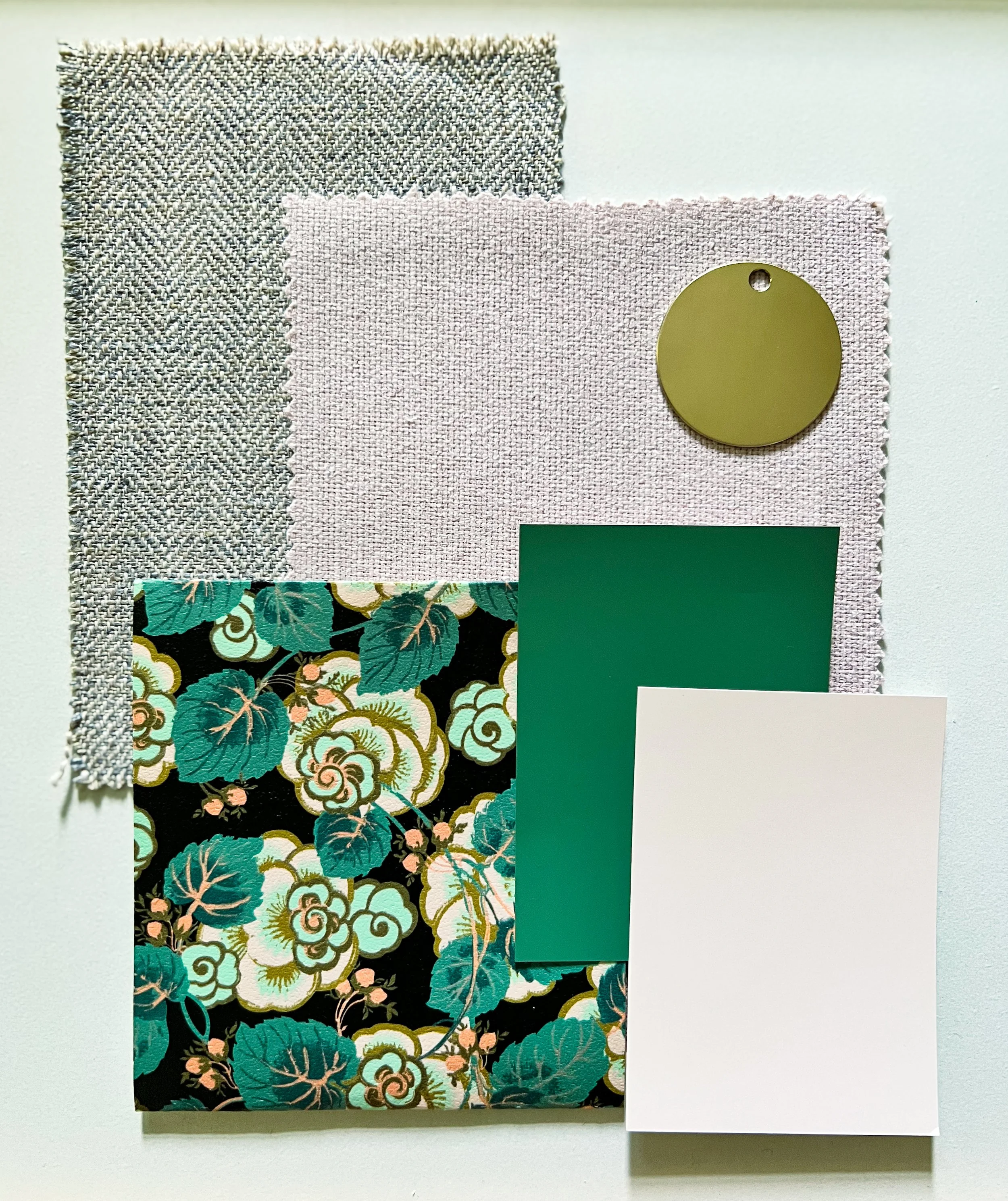 Interior design mood board with gray herringbone fabric, pale pink textile, floral wallpaper, green paint swatch, pink paint swatch, and gold circular sample of hardware