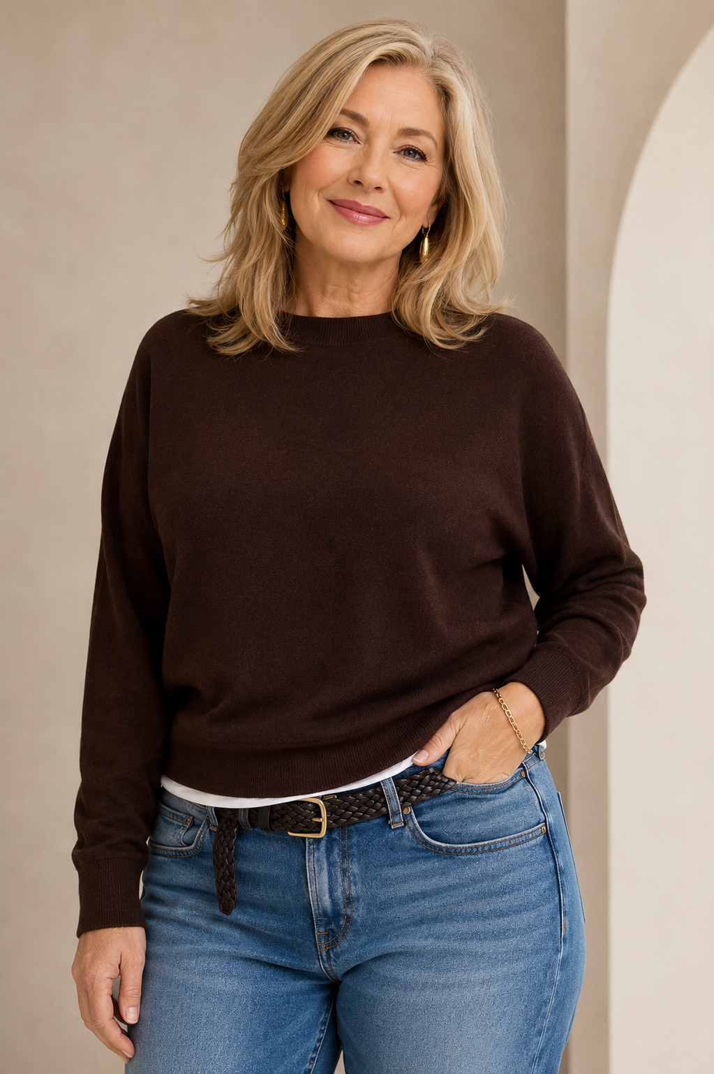 Woman in her 60s wearing a brown sweater with jeans.
