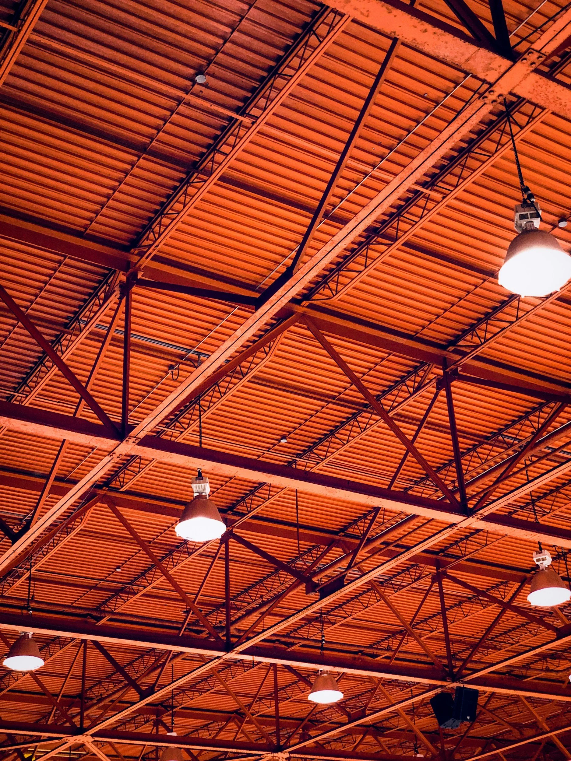 Ceiling of a large indoor space with a wooden slat design, metal beams, and hanging light fixtures.