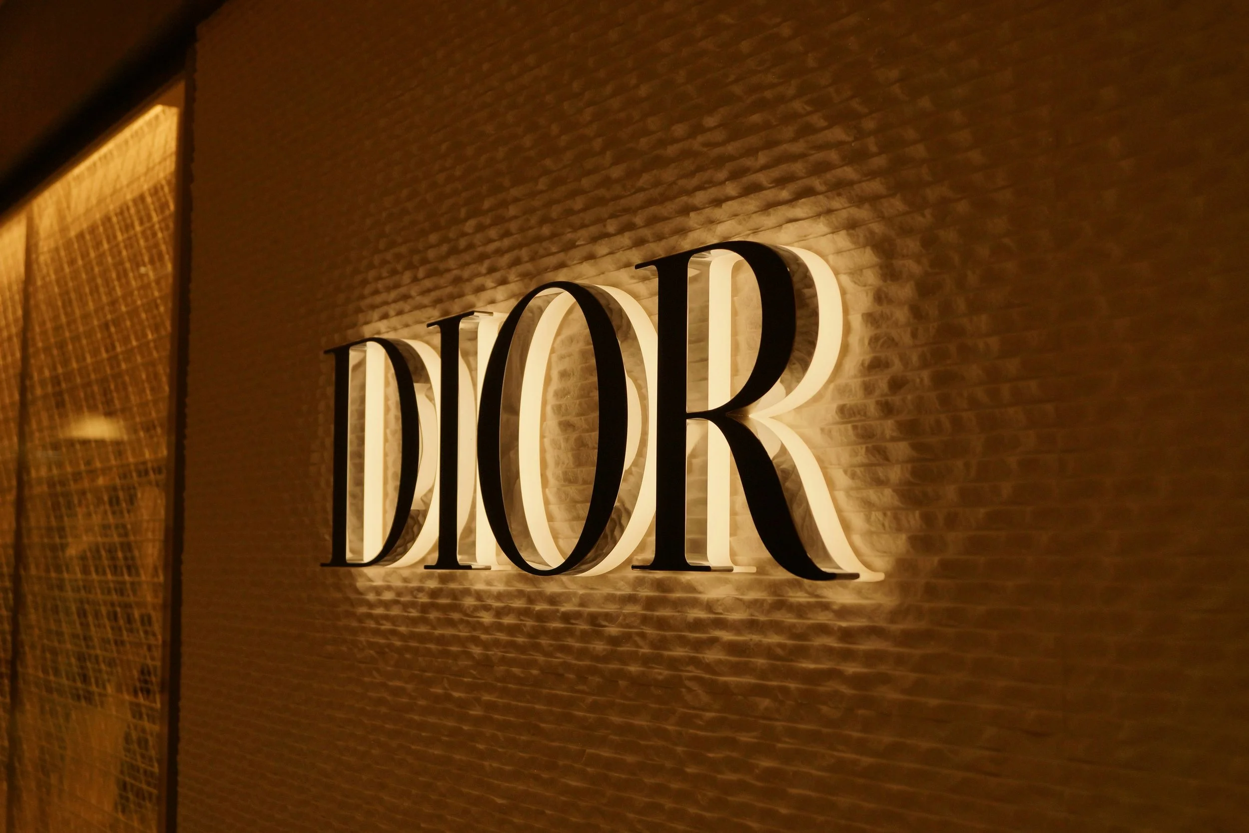 Close-up of a glowing 'Dior' sign mounted on a brick wall, with soft warm lighting highlighting the signage.