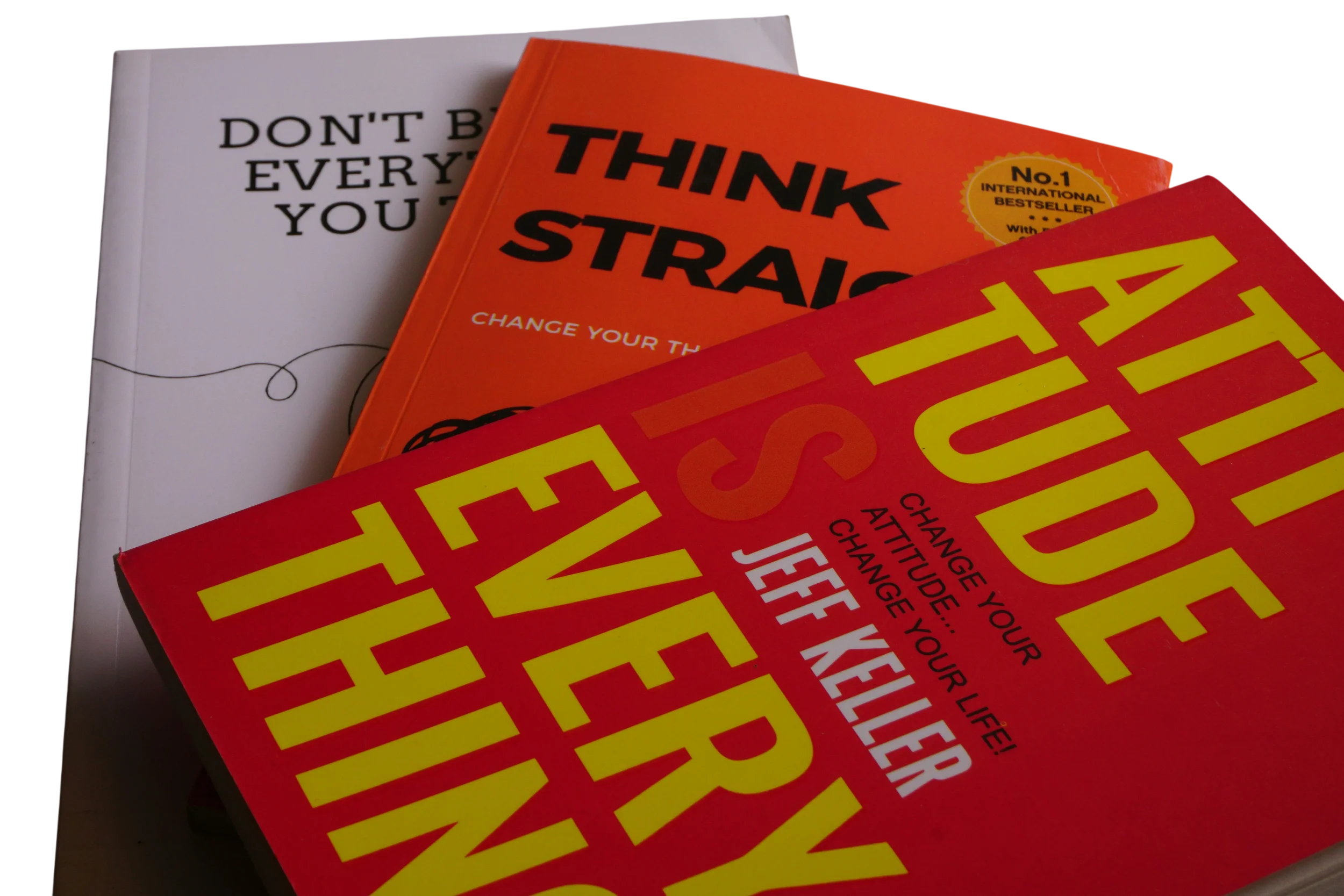 Close-up of three books stacked on a white surface, with the middle book titled 'THINK STRAIGHT' in bold black letters on an orange cover, and the bottom book with large yellow and red text.
