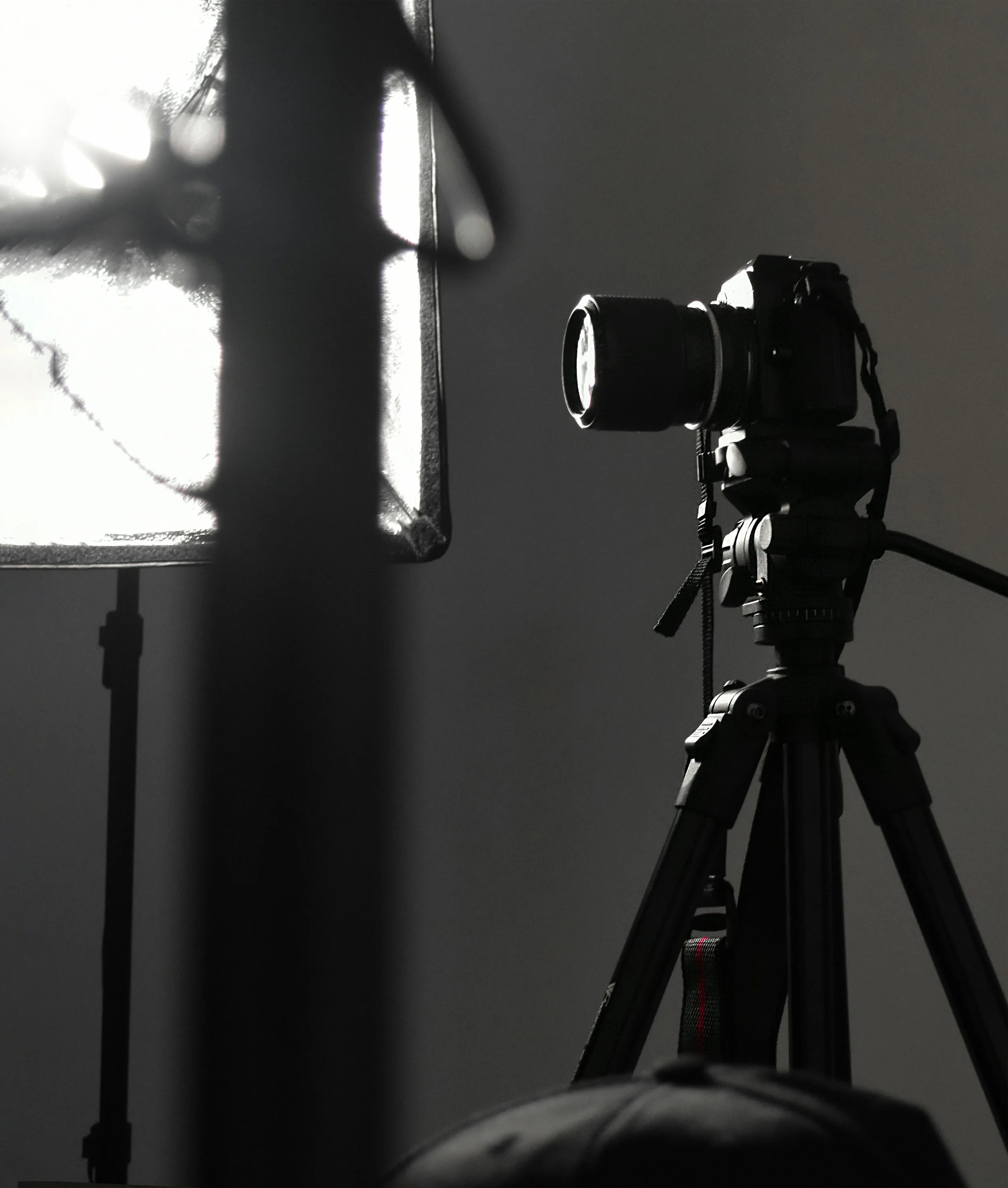 A professional camera mounted on a tripod with a lens, facing a black surface. A bright light source casts shadow and reflections on the objects and background.